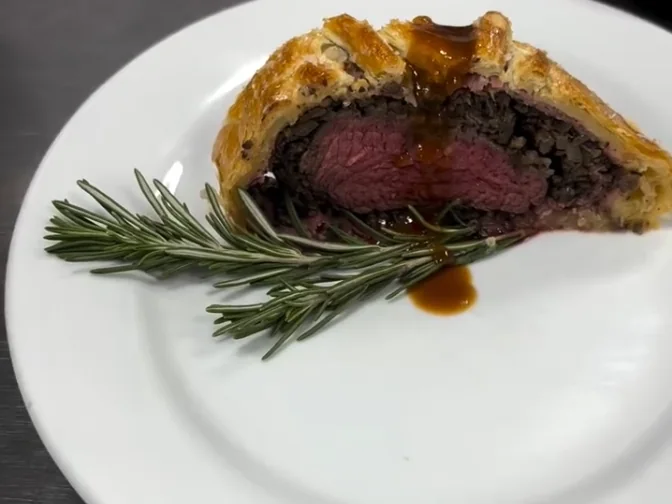 Beef Wellington sliced to show the pink center, with rosemary and jus