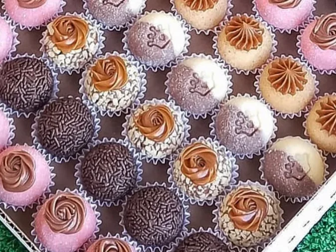 A box of brigadeiros in pink, chocolate, and chopped nuts